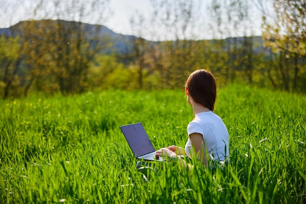 Photo femme utilisant un ordinateur portable alors qu'elle est assise sur le terrain