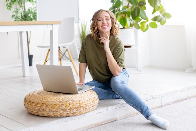 Femme utilisant un ordinateur portable alors qu'elle était assise au sol à l'intérieur de la maison. Femme indépendante travaillant à domicile Étudiante à distance relaxante et leçons de surveillance en vidéoconférence