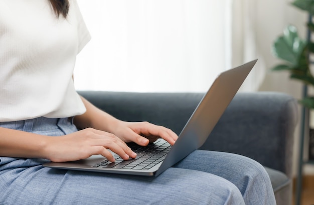 Femme utilisant un ordinateur portable assis sur un canapé dans le salon.