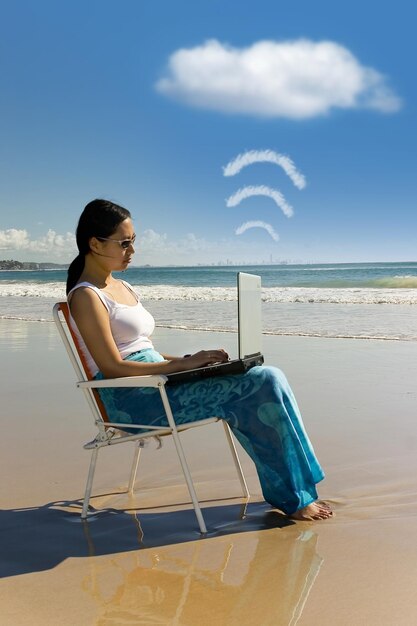 Photo femme utilisant un ordinateur portable assise sur une chaise à la plage contre le ciel