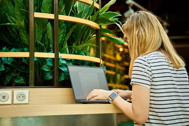 Femme utilisant un ordinateur portable en coworking avec des plantes vertes