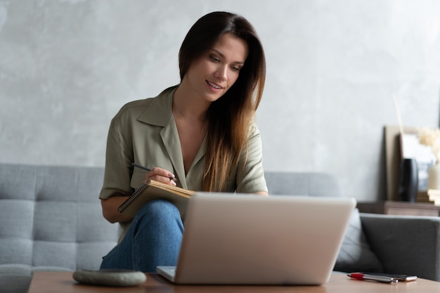 Femme utilisant un ordinateur portable dans son salon. Travail à domicile pendant le confinement. Distanciation sociale.