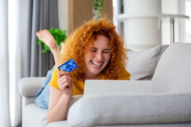 Femme utilisant un ordinateur portable faisant des achats en ligne en utilisant une carte de crédit jouant en ligne en souriant à l'intérieur