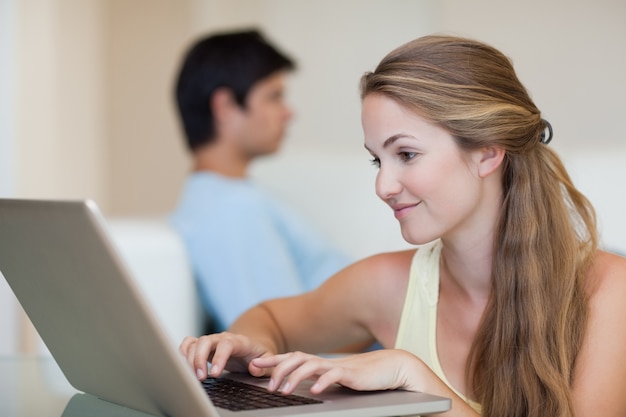 Femme utilisant un ordinateur portable pendant que son fiancé est assis sur un canapé