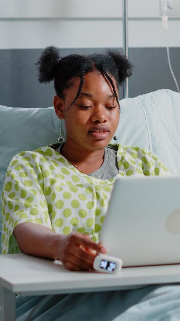 Femme Utilisant Un Ordinateur Portable Pour Parler à Des Amis Lors D'un Appel Vidéo Dans Un Lit D'hôpital. Patient Malade Parlant à Des Personnes Lors D'une Conférence à Distance En Ligne En Attendant Qu'un Médecin Fournisse Une Assistance Médicale