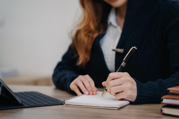 Femme utilisant un ordinateur portable pour travailler et écrire sur un ordinateur portable avec un stylo au bureau