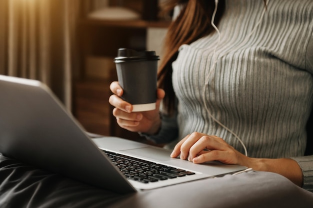 Femme utilisant un ordinateur portable et tapant sur un ordinateur portable et tenant une tasse de café dans le bureau à domicile du café