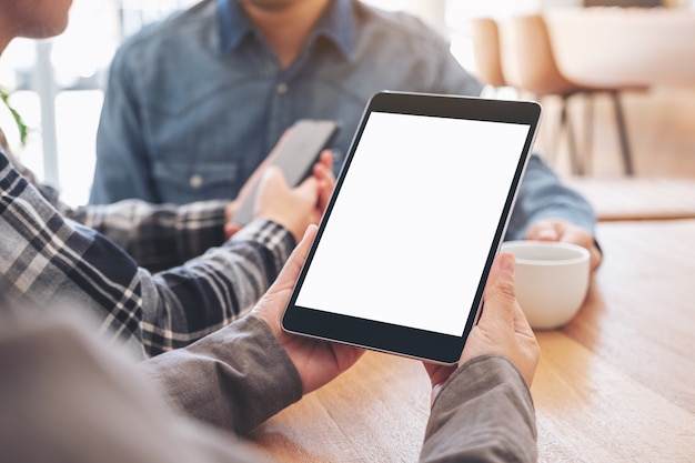 Une femme utilisant et regardant une maquette de tablet pc sur une table en bois avec des amis en arrière-plan