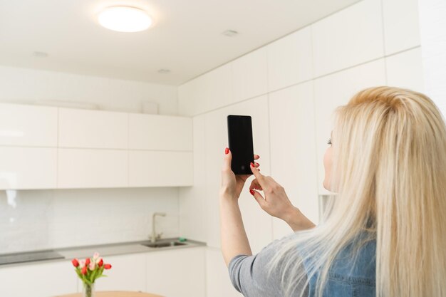 Femme utilisant smartohone dans une maison intelligente, écran vide.