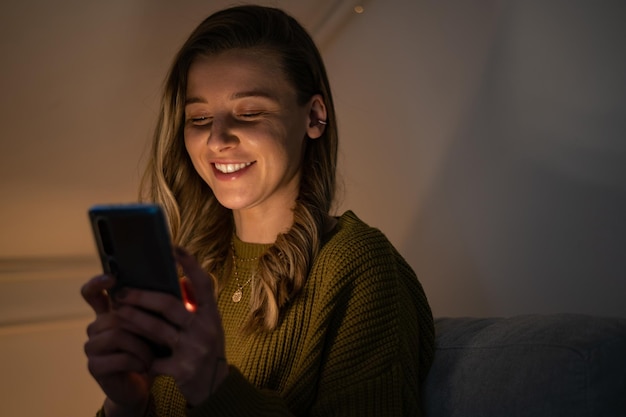 Femme utilisant un smartphone assis sur le canapé à la maison