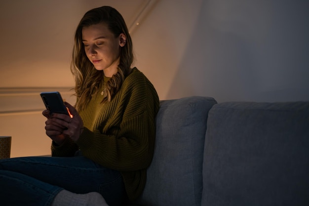 Femme utilisant un smartphone assis sur le canapé à la maison