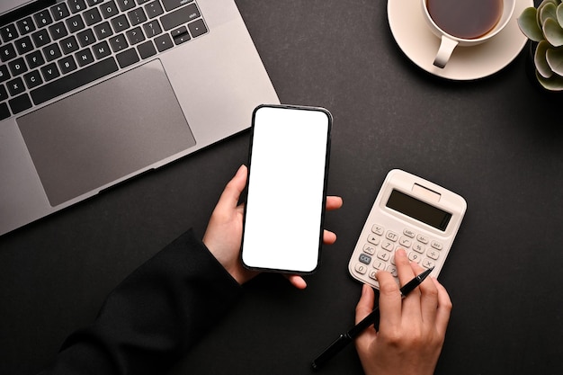 Une femme utilisant un smartphone et une calculatrice dans sa vue de dessus de bureau noir moderne