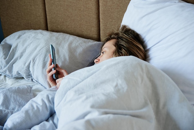Femme utilisant un smartphone dans le lit week-end paresseux des médias sociaux