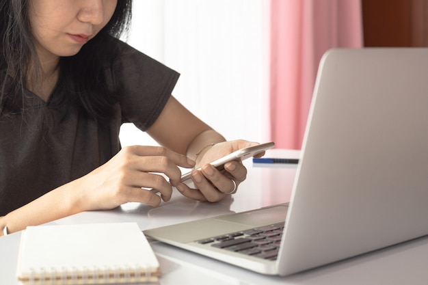 Femme utilisant un smartphone avec un ordinateur portable et travaillant à la maison pour les affaires, l'auto-quarantaine