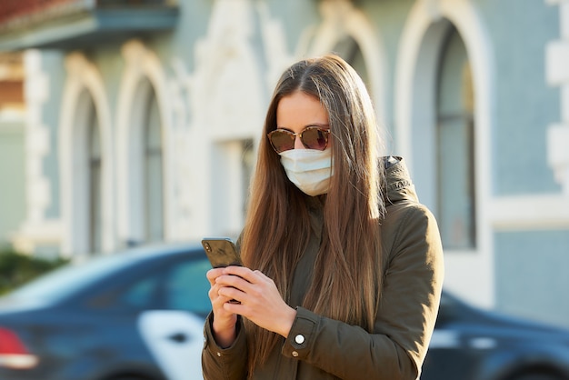 Femme utilisant un smartphone porte un masque médical pour éviter la propagation du coronavirus dans une rue de la ville