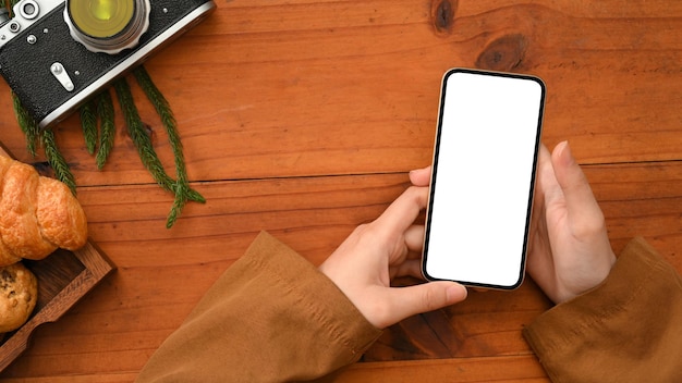 Femme utilisant un smartphone sur une table en bois smartphone écran blanc maquette vue de dessus