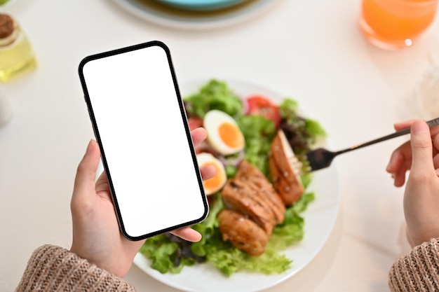 Femme utilisant un smartphone tout en mangeant une salade de poulet grillé biologique saine