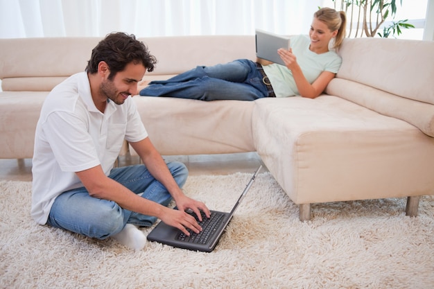 Femme utilisant une tablette alors que son petit ami utilise un ordinateur portable