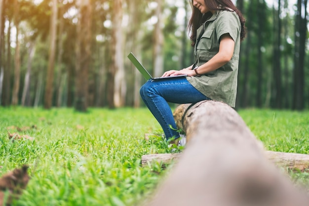 Une femme utilisant et tapant sur le clavier d'un ordinateur portable alors qu'elle était assise sur une bûche dans le parc