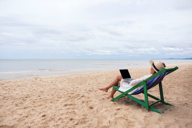 Une femme utilisant et tapant sur un ordinateur portable en position couchée sur une chaise de plage