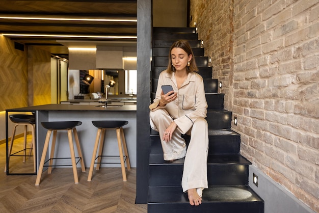 Femme utilisant un téléphone assis dans les escaliers d'un appartement moderne