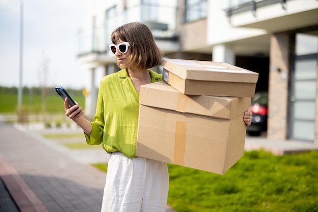 Femme utilisant un téléphone debout avec des colis dans une rue à l'extérieur