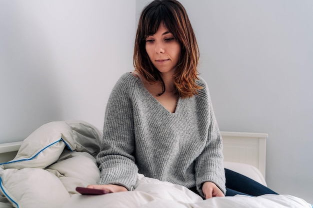 Femme utilisant un téléphone intelligent alors qu'elle est assise sur le lit