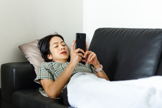 Femme utilisant un téléphone intelligent en position couchée sur le concept de quarantaine du canapé