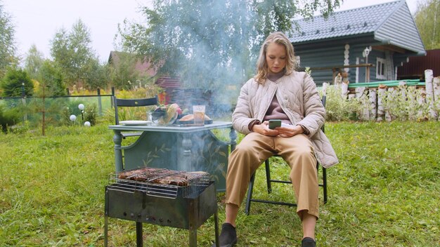 Photo femme utilisant un téléphone portable tout en préparant de la nourriture dans la cour