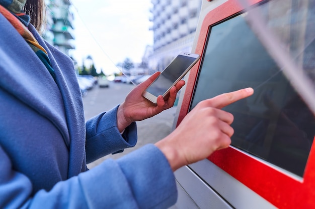 Photo femme utilisant le terminal libre-service de la rue et le smartphone pour payer les services