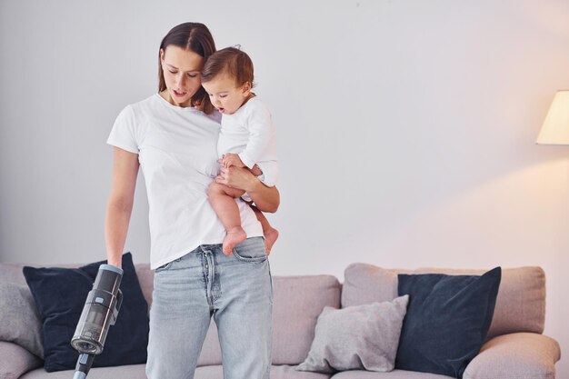 Femme utilise un aspirateur Mère avec sa petite fille est à l'intérieur à la maison ensemble