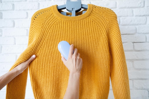 Photo femme utilise une machine pour enlever les granulés et les bobines des vêtements et du tissu sur le pull jaune