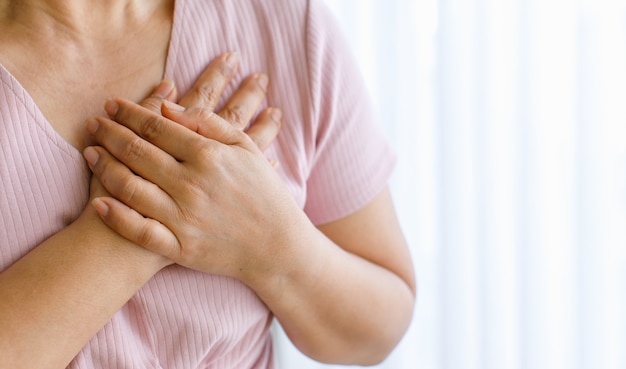 Une femme utilise la main pour se trouer la poitrine avec douleur et souffre d'une maladie cardiaque. Concept d'infarctus du myocarde surélevé ST, avec espace de copie.