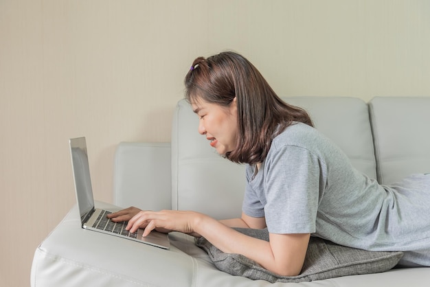 Une femme utilise un ordinateur portable sur un canapé, regarde le réseau social Internet