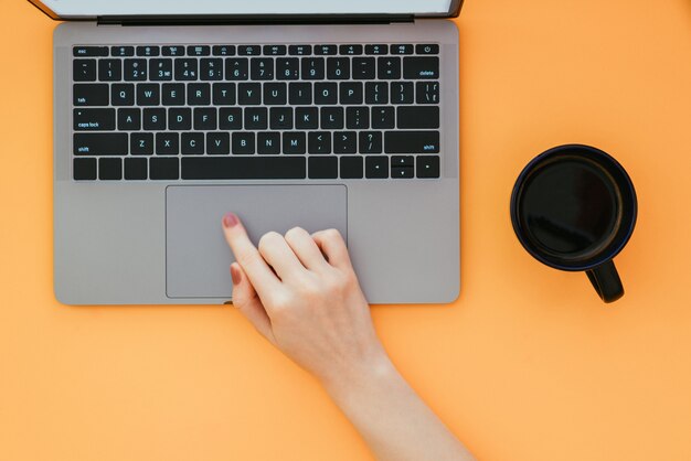 Femme utilise un ordinateur portable sur une surface orange, une tasse de café debout sur la table