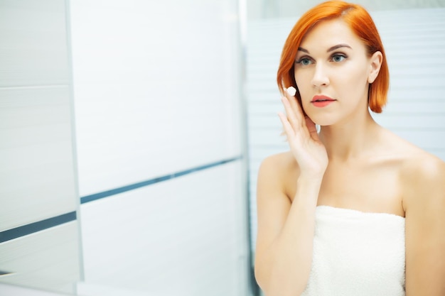 Une femme utilise des produits de soins de la peau à la maison dans une salle de bain lumineuse