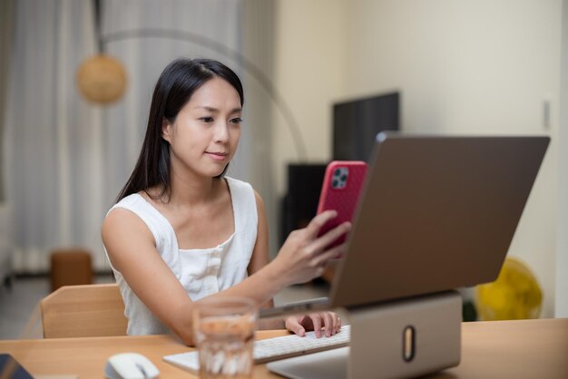 Une femme utilise son téléphone portable pour payer ses achats en ligne sur son ordinateur portable