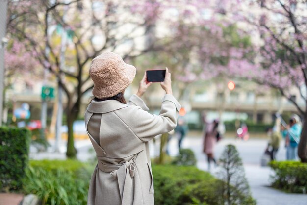 Une femme utilise son téléphone portable pour prendre une photo de l'arbre de sakura
