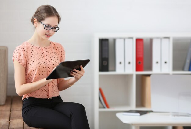 Femme utilise une tablette assise sur le rebord de la fenêtre à la maison