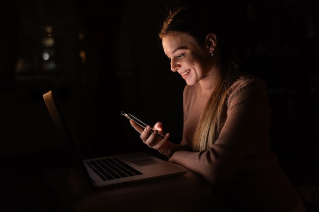 Femme utilise un téléphone portable avec un ordinateur portable tard dans la soirée