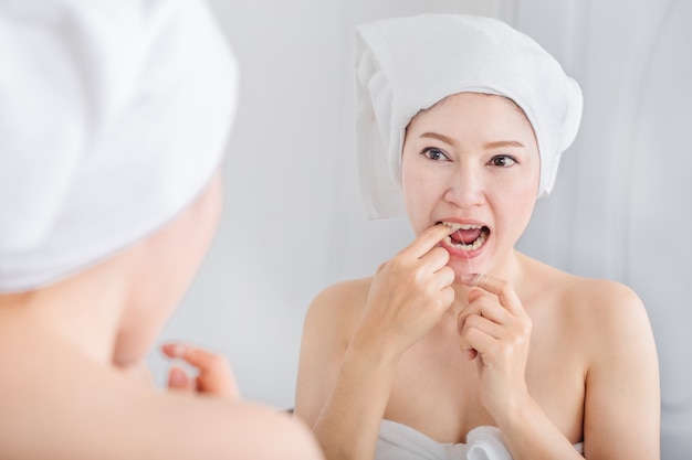 femme utiliser soie dentaire blanc sain avec miroir dans la salle de bain