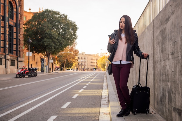 Femme avec valise en attente d'un taxi dans la rue