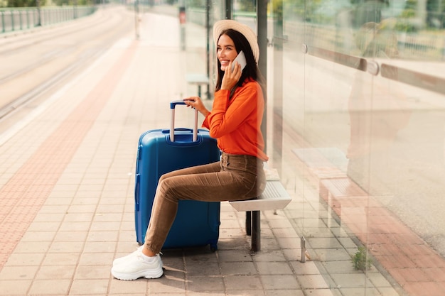 Une femme avec une valise qui parle au téléphone en attendant le train à l'extérieur.