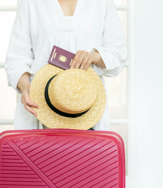 Une femme avec une valise rose tient un chapeau d'été et un passeport roumain et est prête à voyager.