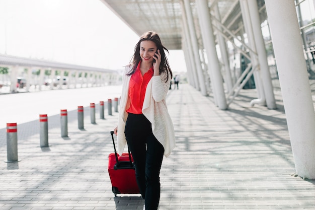 Une femme avec une valise rouge marche le long de l&#39;aéroport et parle au téléphone