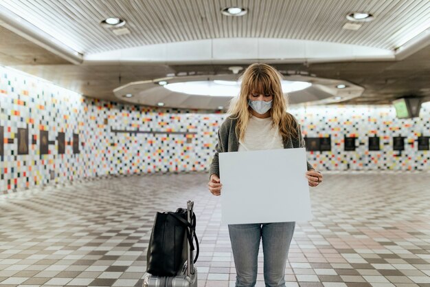 Femme avec une valise tenant un papier vierge pendant l'épidémie de coronavirus