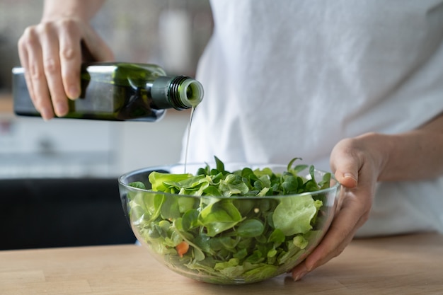 Femme végétalienne cuisine salade avec des légumes frais, des herbes à la cuisine à domicile. Ajouter de l'huile d'olive dans un bol.