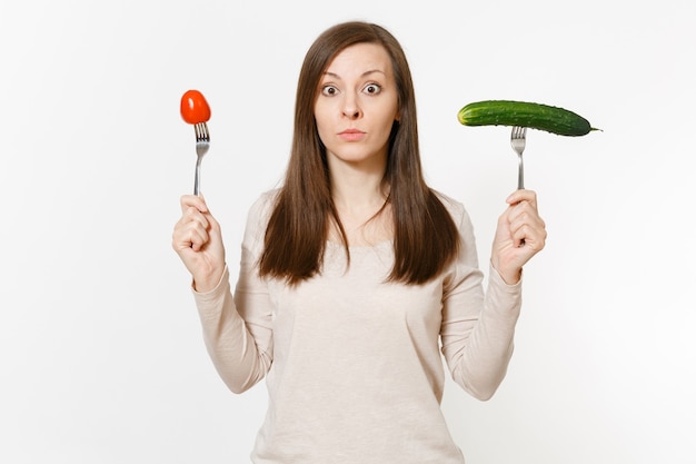 Une femme végétalienne irritée tient un concombre vert, une tomate rouge sur une fourchette isolée sur fond blanc. Bonne nutrition, nourriture végétarienne, mode de vie sain, concept végétal. Zone publicitaire avec espace de copie.