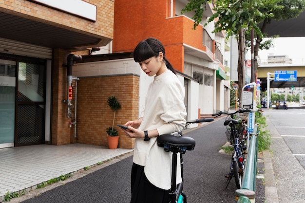 Photo femme avec vélo électrique dans la ville à l'aide de smartphone