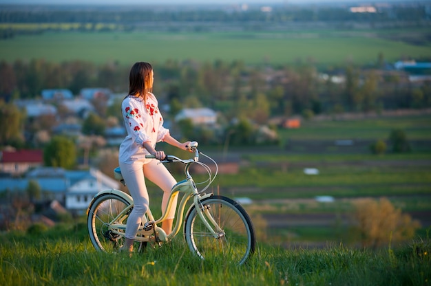 Femme avec vélo rétro sur la colline le soir